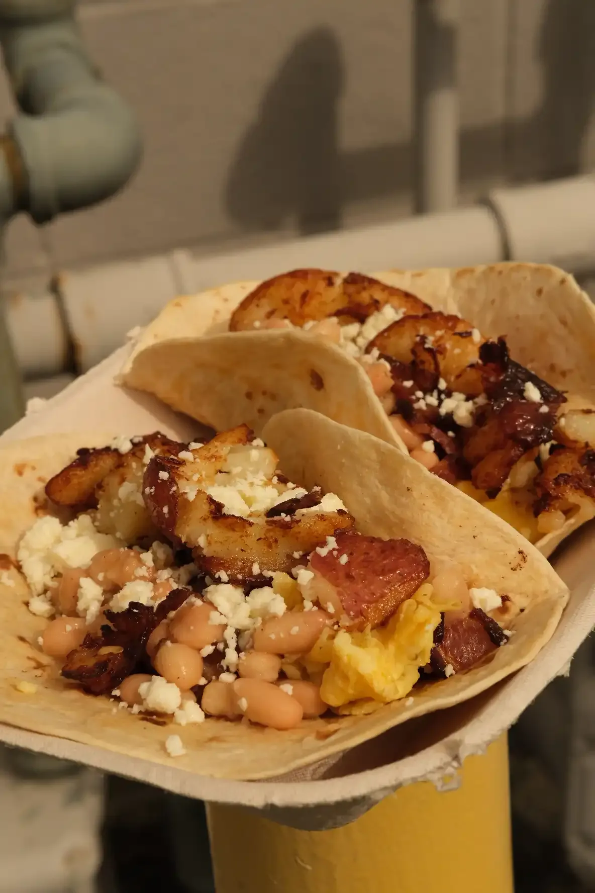 Two breakfast tacos in a paper boat filled with scrambled egg, white beans, bacon, crispy potato and queso fresco